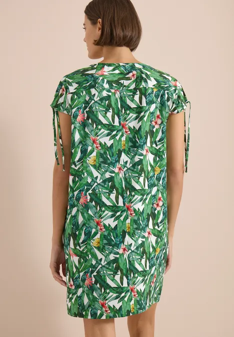 Knielanges Kleid mit floralem Muster khaki Frau von hinten in kurz geschnittenem Kleid mit grünem Tropenpflanzenmuster und seitlichen Schleifen.