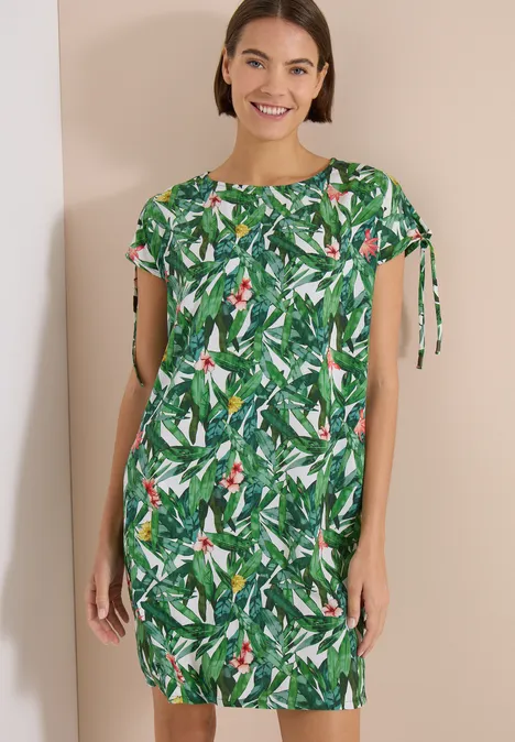 Knielanges Kleid mit floralem Muster khaki Frau trägt ein grünes, kurzärmeliges Kleid mit tropischem Blattmuster.