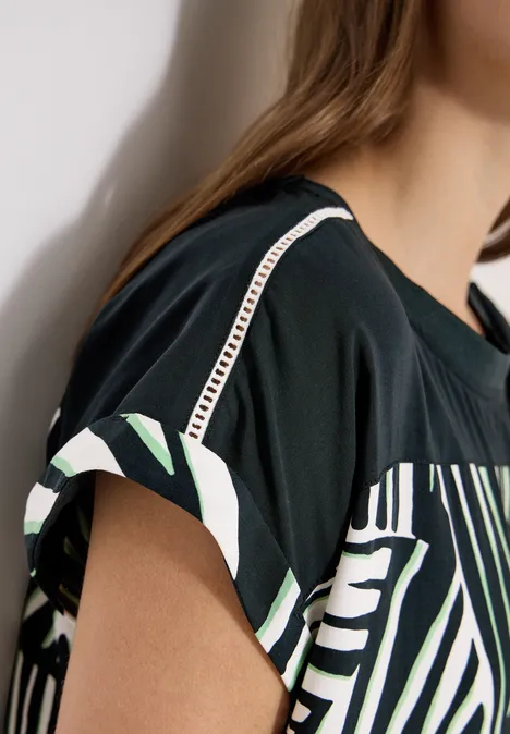 Schwarz-weiß-grünes kurzärmeliges Shirt mit Musterdetail an Ärmeln und Brustbereich.