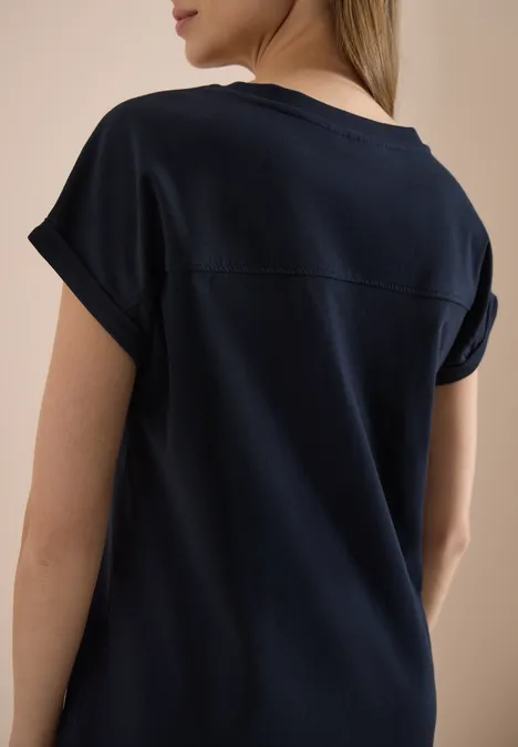 Eine Frau steht mit dem Rücken zur Kamera und trägt ein dunkelblaues T-Shirt.