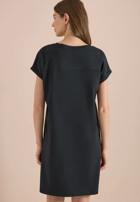 Rückenansicht einer Frau in schlichtem, knielangem schwarzen Kurzarmkleid.