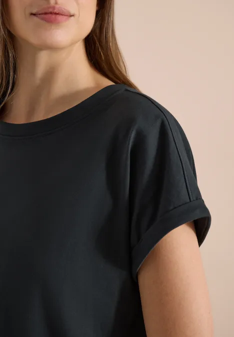 Nahaufnahme eines weiblichen Oberkörpers in schlichtem schwarzem T-Shirt mit kurz umgeschlagenen Ärmeln.