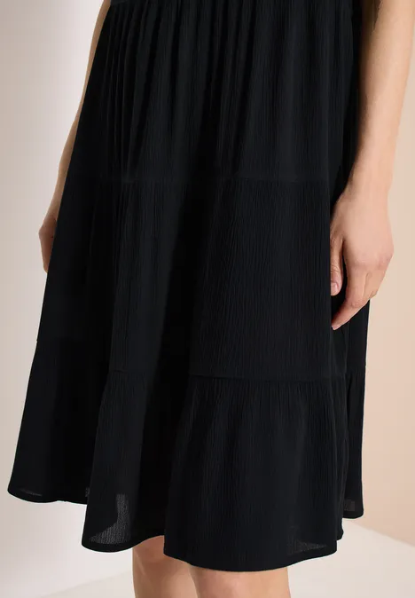 Schwarzes, knielanges Stufenkleid aus leichtem Stoff.