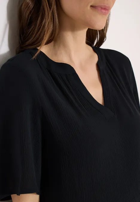 Schlichte, schwarze Damenbluse mit V-Ausschnitt und kurzen Ärmeln, nah am Oberkörper.