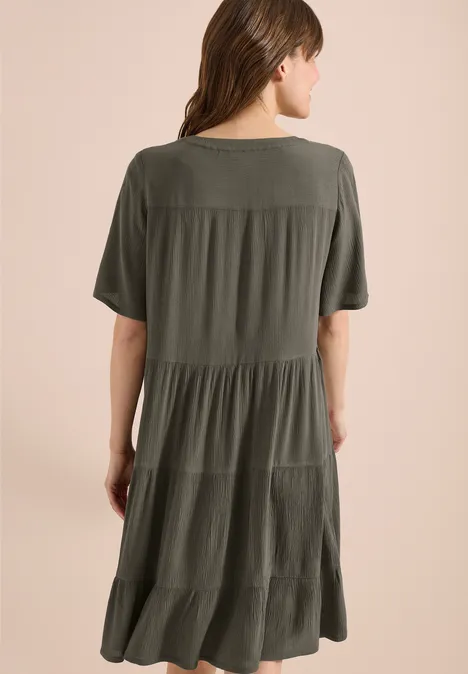 Frau in locker sitzendem, stufigem Midikleid in Olivgrün mit kurzen Ärmeln, Rückenansicht.