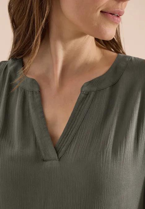 Detail eines dunkelgrauen, strukturierten V-Ausschnitt-Blusentops an einer Frau.