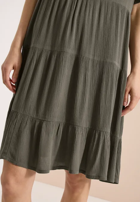 Olivegrünes, knielanges Stufenkleid aus leichtem Stoff mit Rüschenbesatz.