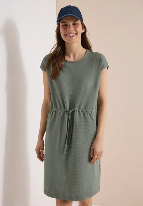 Knielanges Kleid aus Jersey khaki Frau in legerem, knielangem, khakigrünem T-Shirt-Kleid mit Taillenschnur vor neutralem Hintergrund.