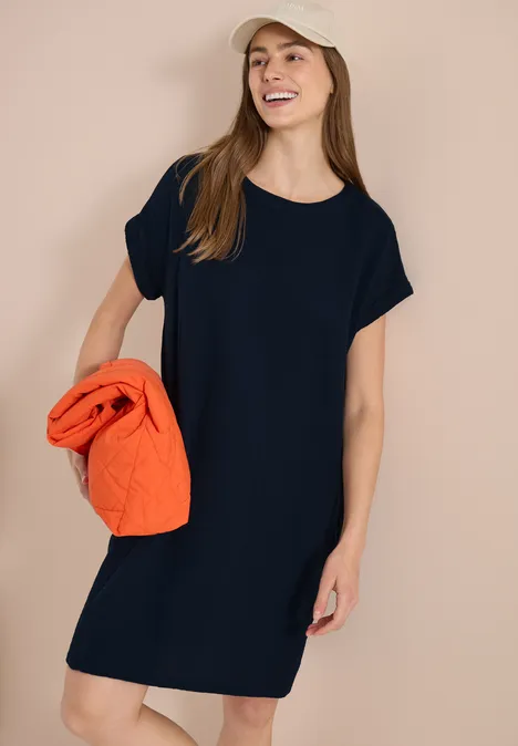 Femme en robe noire à manches courtes tenant un pull orange