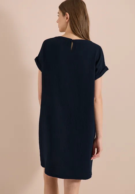 Une femme vue de dos porte une robe droite bleu foncé à manches courtes.