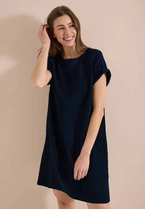 Femme en robe t-shirt bleu foncé décontractée sur fond beige uni.