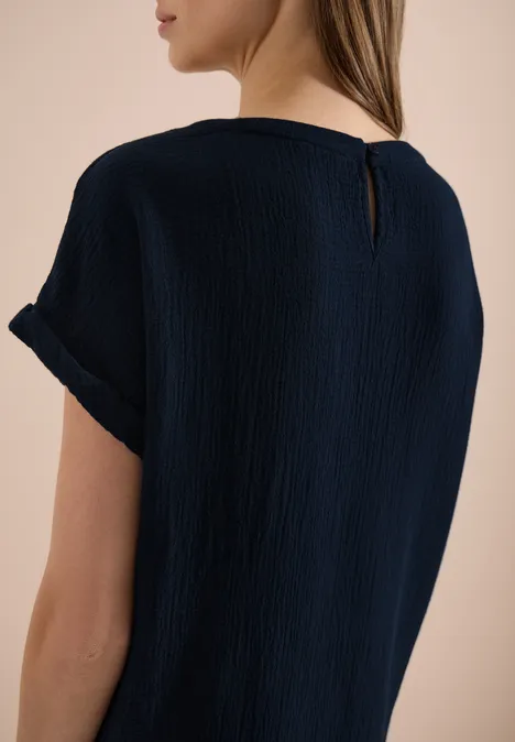 Femme de dos portant un haut bleu marine à manches courtes texturé et revers de manches.