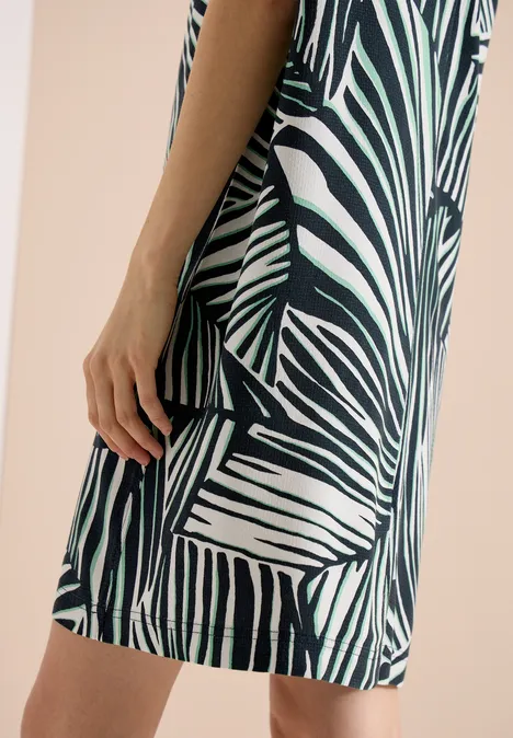 Eine Frau trägt seitlich stehend ein kurz geschnittenes, grün-weiß gestreiftes Kleid im Zebramuster.