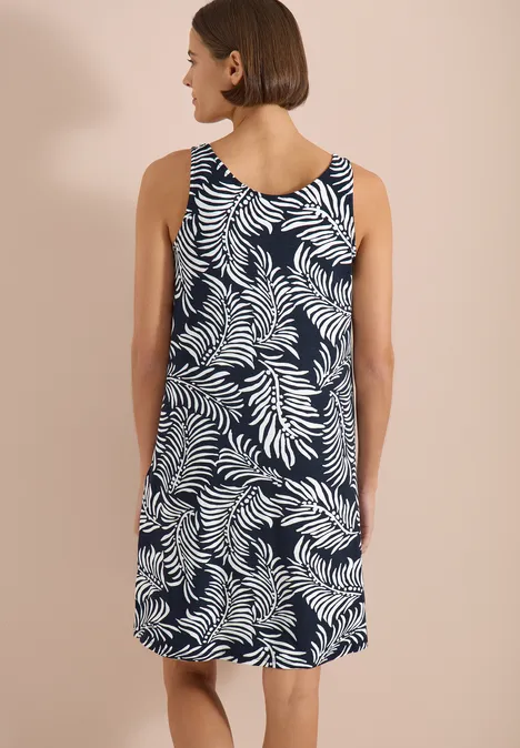 Rückansicht einer Frau in ärmellosem Kleid mit blauem Grund und weißem Blattmuster.