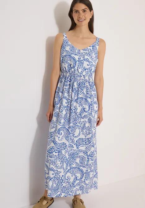 Robe longue à encolure en V et imprimé vanilla white Une femme porte une robe longue sans manches blanche à motif paisley bleu.