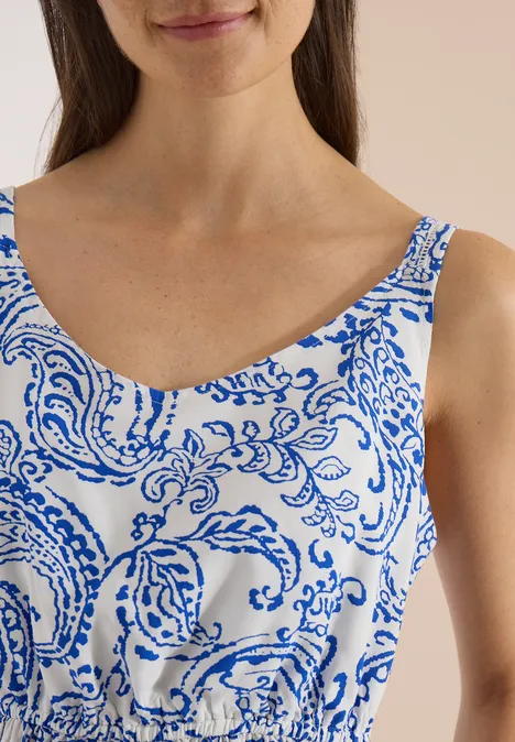 Robe longue à encolure en V et imprimé vanilla white Une femme porte un haut sans manches blanc à motifs bleus ornementaux et à encolure arrondie.