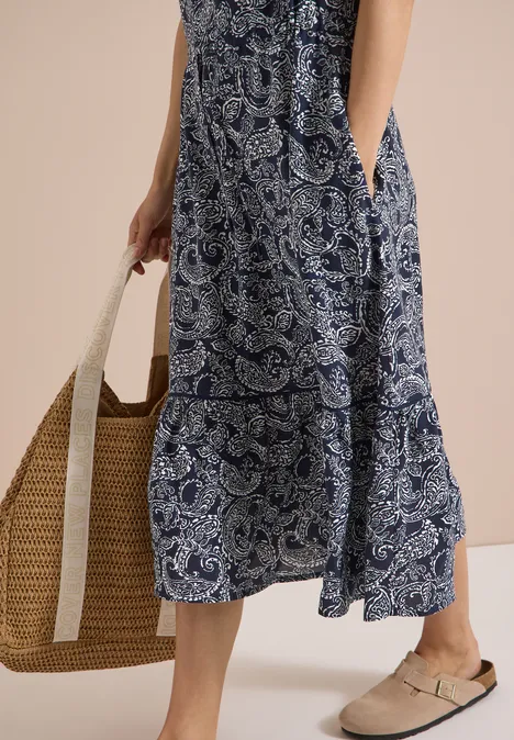 Midikleid mit Split Neck und Print universal blue Frau in blau-weißem Paisley-Kleid trägt einen geflochtenen Strohbeutel und bequeme Slipper.