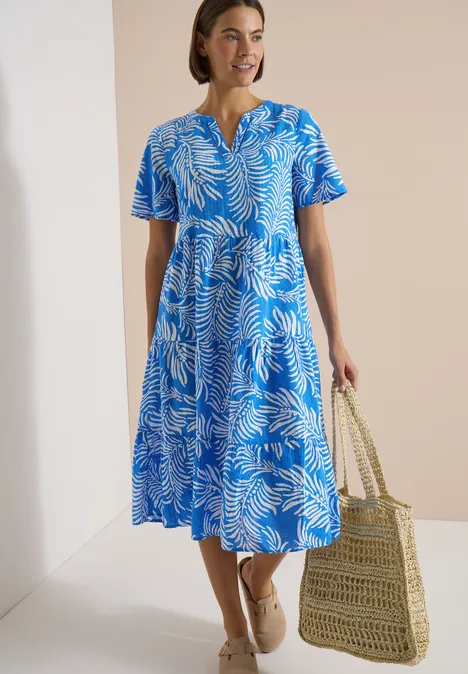 Midikleid mit Split Neck und Print ethereal blue Frau in midilangen blau-weißem Blattmuster-Kleid, V-Ausschnitt, trägt Strohtasche und bequeme Sandalen.