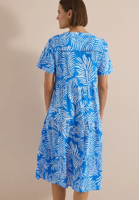 Midikleid mit Split Neck und Print ethereal blue Eine Frau steht mit dem Rücken zur Kamera und trägt ein blau-weißes, kurzärmeliges, knielanges Kleid mit Blattmuster.