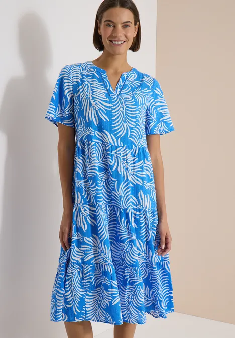 Midikleid mit Split Neck und Print ethereal blue Frau trägt blaues Midikleid mit weißem Blattmuster, steht vor neutralem Hintergrund