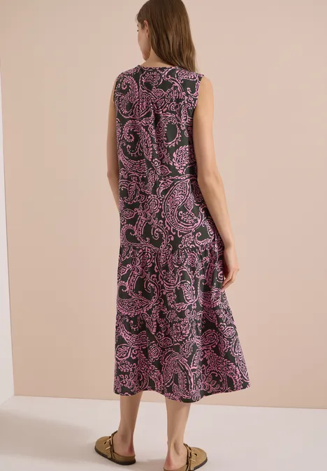 Eine Frau trägt ein ärmelloses Midikleid mit schwarzem Grund und pinkem Paisley-Muster, Rückansicht.