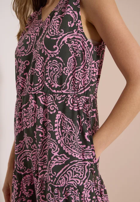 Eine Frau trägt ein ärmelloses Kleid mit pinkem Paisley-Muster auf dunklem Stoff.