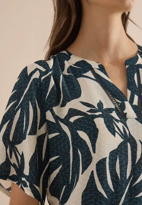 Femme portant un chemisier clair à motifs de feuilles tropicales foncées, col en V, mise au point sur le tissu.