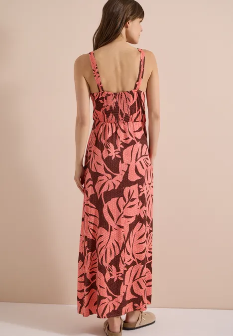 Femme vue de dos portant une longue robe sans manches à imprimé feuilles corail