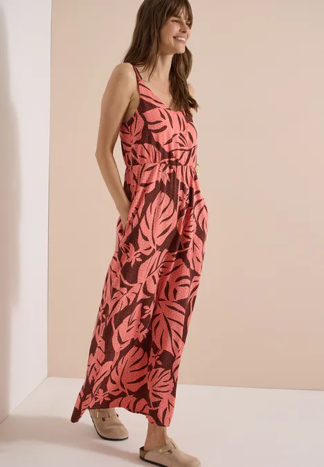 Femme en combinaison rouge à motifs feuilles noirs et baskets blanches devant un mur clair.