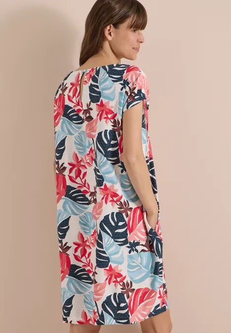 Vrouw van achteren in losse midi-jurk met korte mouwen en kleurrijk bladerenpatroon.