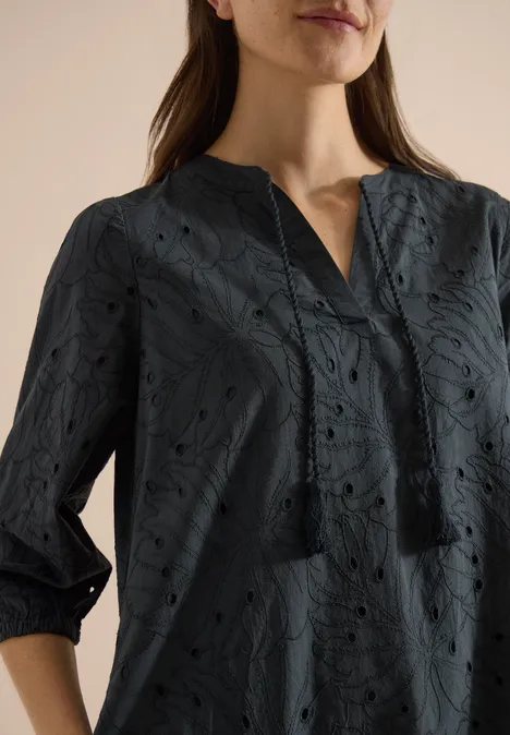 Robe longueur genou avec manches 3/4 et broderie palm breeze green Une femme porte un chemisier bleu foncé à motifs découpés floraux, manches 3/4 et col en V.