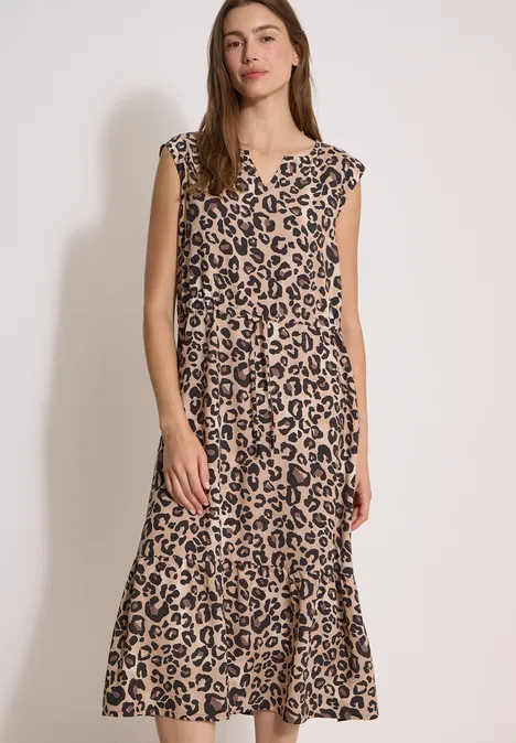 Frau in knielangem Kleid mit Leopardenmuster und kurzen Ärmeln vor hellem Hintergrund.