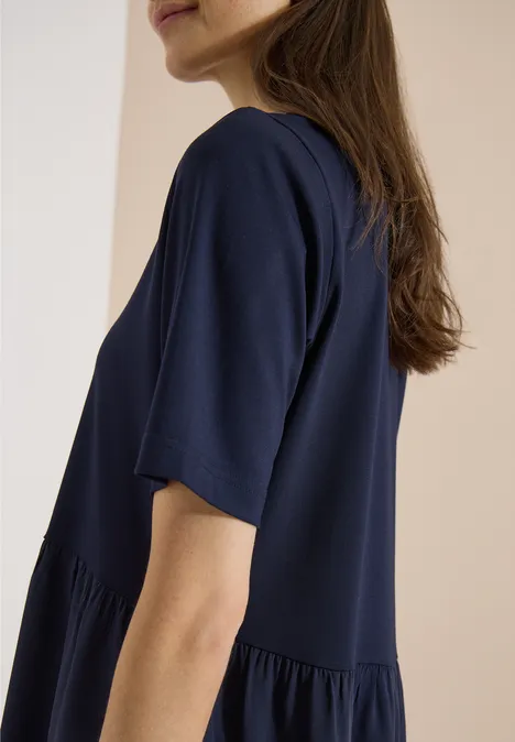 Frau in locker sitzendem dunkelblauem T-Shirt vor hellem Hintergrund