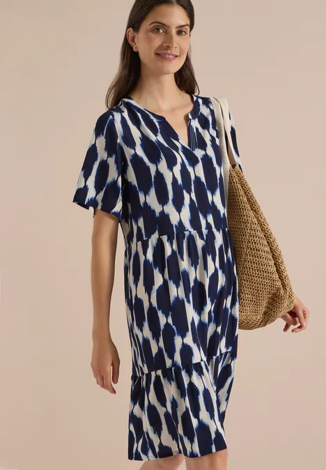 Knielanges Kleid mit Split Neck und Struktur urban dark blue Frau trägt blau-weiß gemustertes V-Ausschnitt-Kleid mit kurzen Ärmeln und Strohtasche