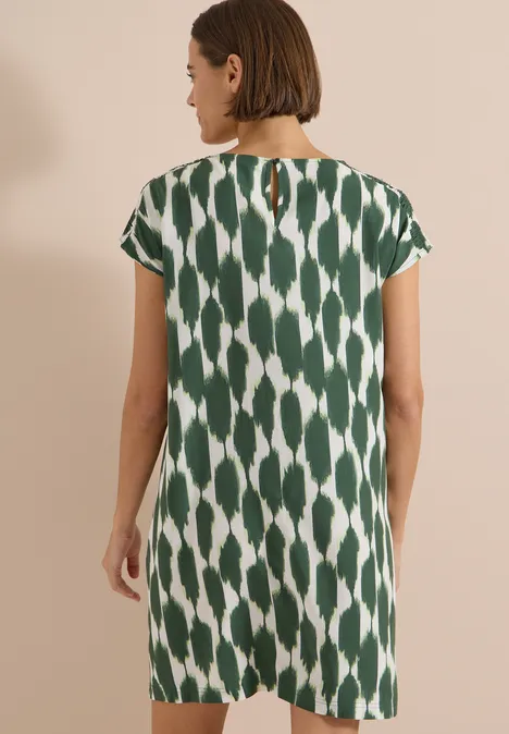 Frau in grün-weiß gemustertem, knielangem, kurzärmligem Kleid mit kleinem Rückenschlitz.