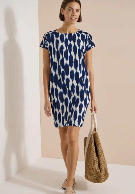 Frau in blau-weiß gemustertem kurzärmeligem Kleid mit Korbtasche.