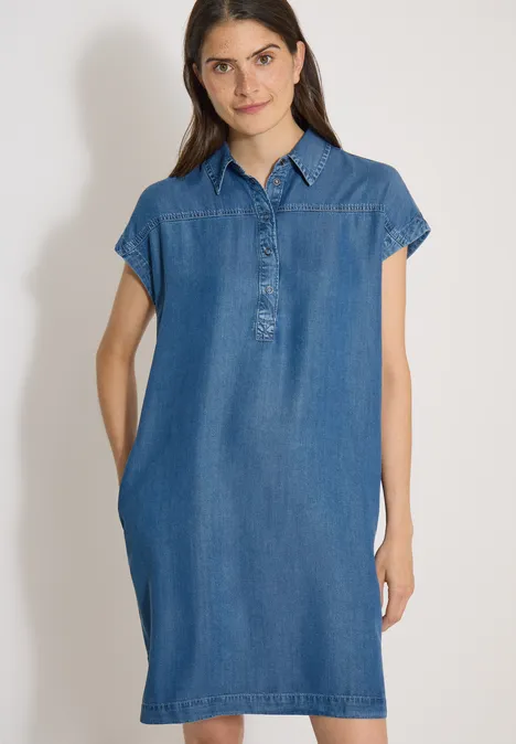 Vrouw in eenvoudige denimjurk met korte mouwen, overhemdkraag en zijzakken.