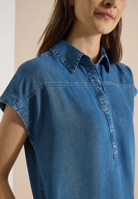 Vrouw in mouwloos spijkerblouse met hoge kraag en een kort knoopsluiting.