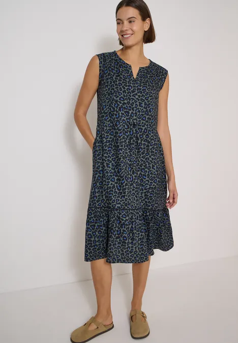 Midikleid mit Split Neck und Print dried olive green Frau in ärmellosem, dunkelblauem Midikleid mit kleinem Muster, gestufter Rockpartie und beigen Loafern.