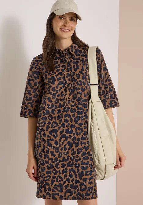 Knie-lange corduroyjurk met luipaardprint creamy mocha Frau in braun-schwarzem Leoprint-Kleid mit halblangen Ärmeln, Cap und großem cremefarbenem Shopper, lächelt.
