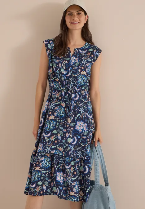 Midikleid mit Split Neck und Print urban dark blue Frau in geblümtem blauem Midikleid mit Rüschensaum und Cap, hält hellblaue Tasche