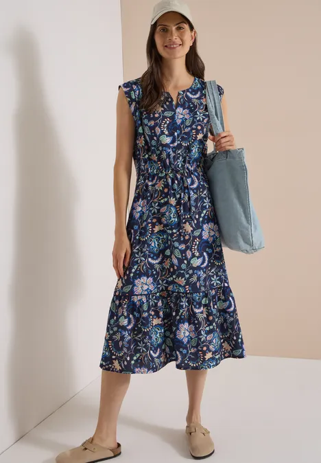 Midikleid mit Split Neck und Print urban dark blue Frau im blauen, gemusterten Midikleid mit weißen Sneakern und Cap, die eine blaue Tasche trägt.