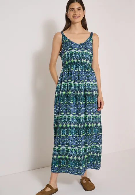 Maxikleid mit V-Neck und Print urban dark blue Frau in ärmellosem blau-grün gemustertem Maxikleid mit Taschen, lächelnd vor weißem Hintergrund.