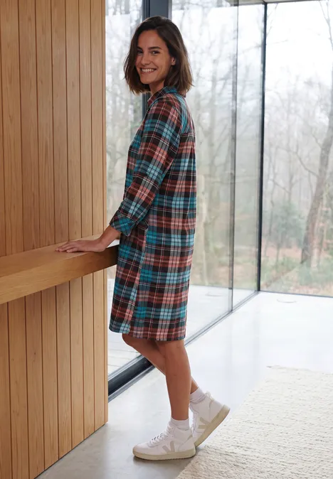 Knielanges Flanellkleid mit Print dark russet red Eine lächelnde Frau in einem karierten Hemdblusenkleid lehnt an einer Holztheke vor großen Glastüren.
