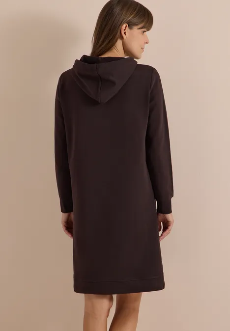 Frau von hinten in einem knielangen, dunkelbraunen Kapuzenkleid mit langen Ärmeln.