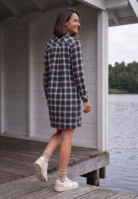 Robe à carreaux arrivant aux genoux urban dark blue Frau in kariertem Hemdblusenkleid steht auf Steg und blickt über ruhigen See.