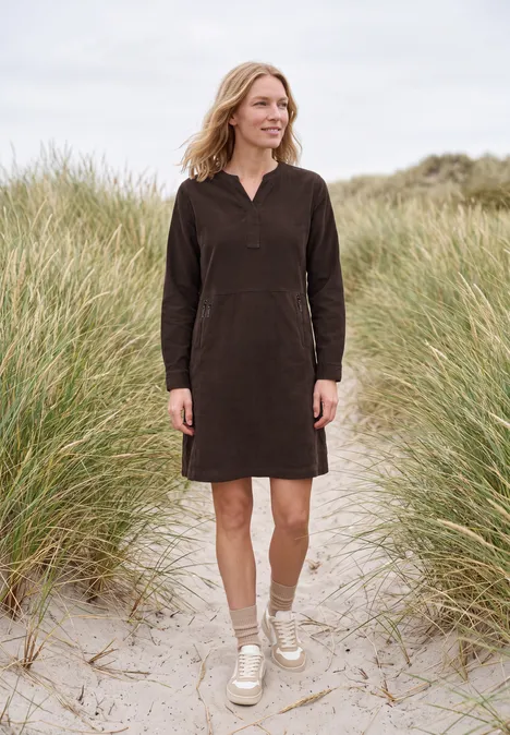 Femme en robe longue marron debout sur une plage sablonneuse avec des dunes