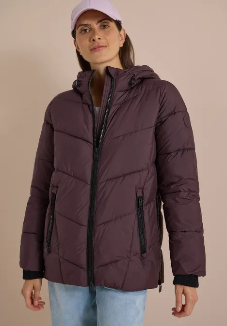 Frau in violettem Steppmantel mit Kapuze und Cap, lässiger Freizeitlook.