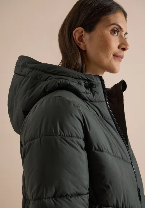 Puffer-Jacke in Midi-Länge mit Kapuze olive night Frau im Profil mit dunkelgrünem, gesteppter Jacke und Kapuze vor neutralem Hintergrund.