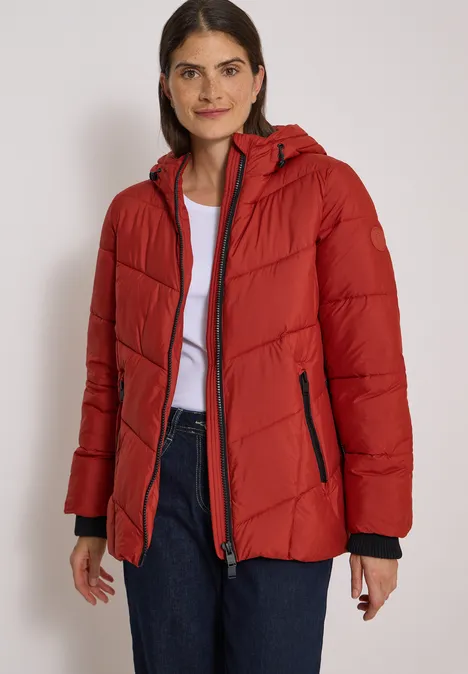 Puffer-Jacke in Midi-Länge mit Kapuze light russet red Frau trägt rote gesteppte Jacke mit Kapuze, weiße Bluse und Jeans, steht vor neutralem Hintergrund.